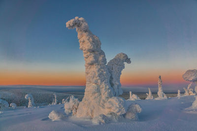 Snow covered land against sky during sunset