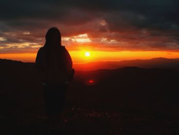 Rear view of silhouette man standing on field against sky during sunset