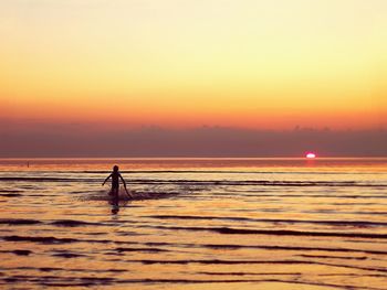 Silhouette person on beach against sky during sunset