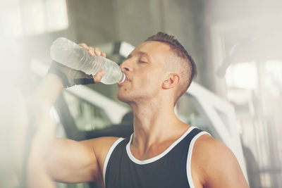 Man drinking water while standing in gym
