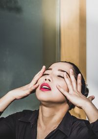 Close-up of young woman touching face by window