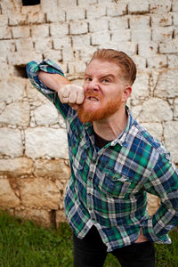 Portrait of man gesturing while making face standing against wall