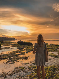 Rear view of woman standing on beach during sunset