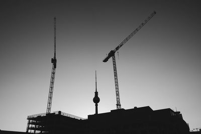 Silhouette cranes and fernsehturm against clear sky