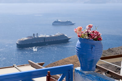 Close-up of a blue vase with flowers on a terrace in santorini with an aerial view of the sea 