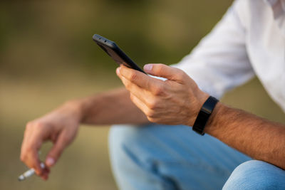 Midsection of man using mobile phone while smoking cigarette outdoors