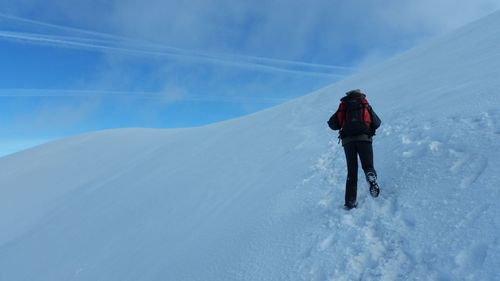 Rear view of man hiking on snow covered mountain against sky