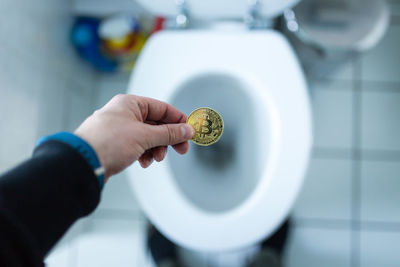 High angle view of person holding bit coin over toilet bowl