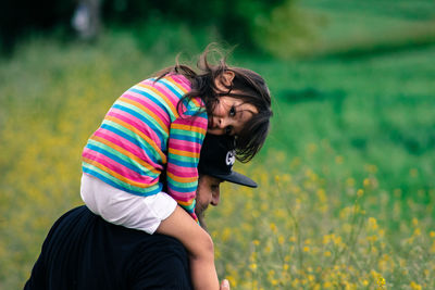 Portrait of girl enjoying ride on shoulder from father in field