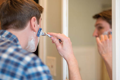 Close-up of young man shaving at home