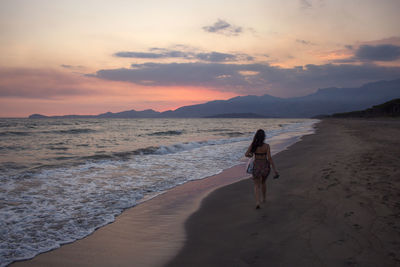 Woman on beach against sky during sunset