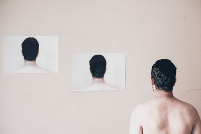 Rear view of shirtless man standing against white wall