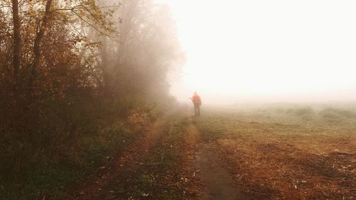 Rear view of man walking on landscape against sky