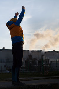 Full length of man stretching arms while standing against factory in city