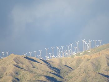 Low angle view of wind turbines on mountains against sky
