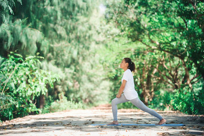 Full length side view of young woman warming up while exercising at park