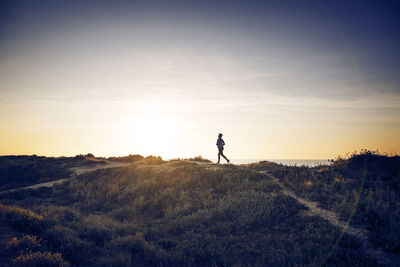 Distant view of woman jogging on field against sky