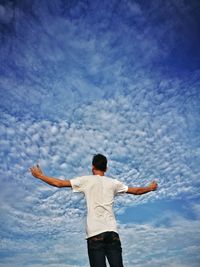 Rear view of man with arms outstretched standing against sky