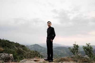 Portrait of young man standing on mountain against sky