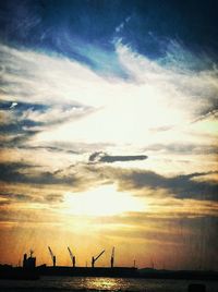 Silhouette cranes in sea against sky during sunset