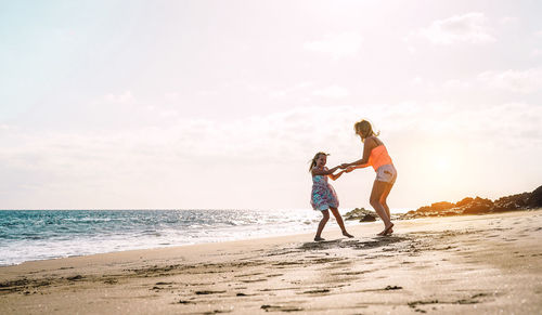 Woman and girl playing at beach against sky during sunset