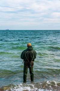 Rear view of man standing in sea against sky