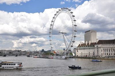 Ferris wheel by river against sky in city