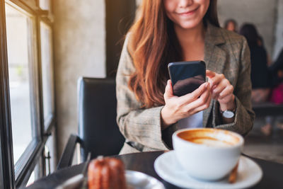 Midsection of businesswoman using mobile phone at coffee shop