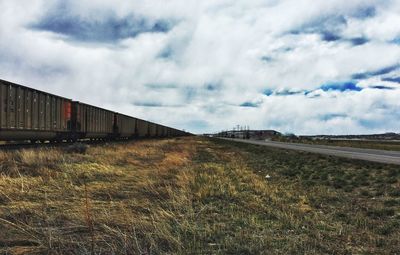 Train by grassy field against cloudy sky