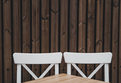 Close-up of chairs and table against wooden wall