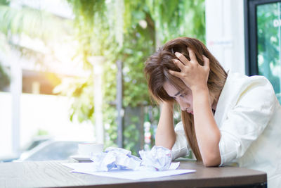 Tensed woman with crumpled papers sitting at cafe