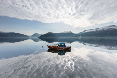 Boat moored in lake against cloudy sky