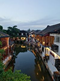 Illuminated buildings by river against sky in city