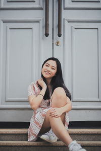 Portrait of smiling woman sitting at entrance of building