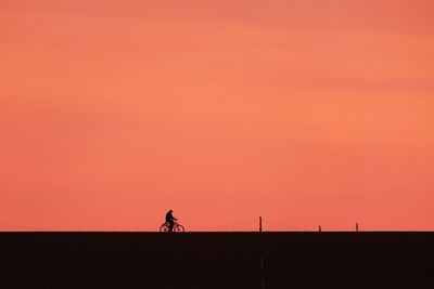 Silhouette people riding on land against orange sky