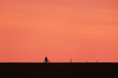 Silhouette man riding bicycle against orange sky