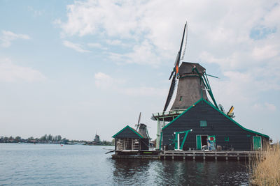 Traditional windmill by lake against sky