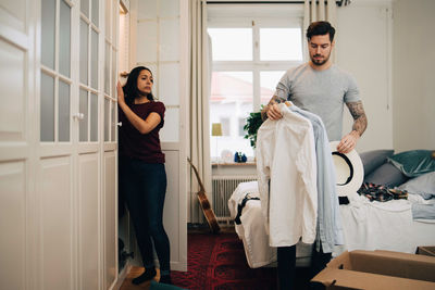 Man holding shirts and hat while standing by woman in new home