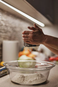 Flour falling through sifting device in woman's hands into big trnsparent glass bowl