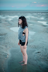 Young woman standing at beach against sky