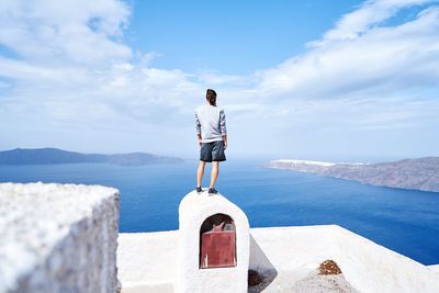 Rear view of man standing by sea against sky