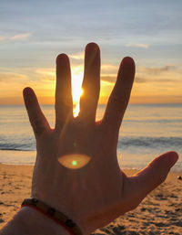 Close-up of hand against sea during sunset