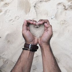 Close-up of hand holding heart shape on sand