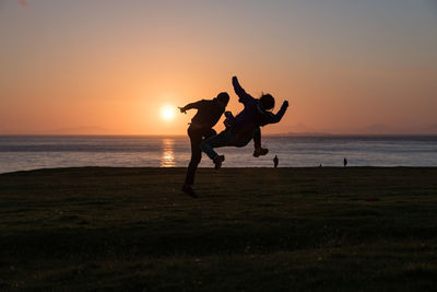 Silhouette friends jumping at beach against clear sky