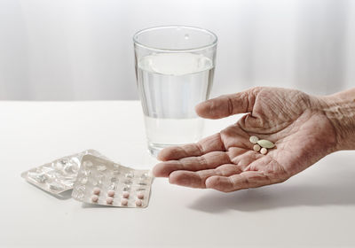 Close-up of wrinkled hand holding medicines on table