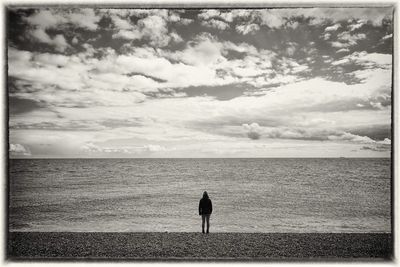 Silhouette of woman standing on beach against cloudy sky