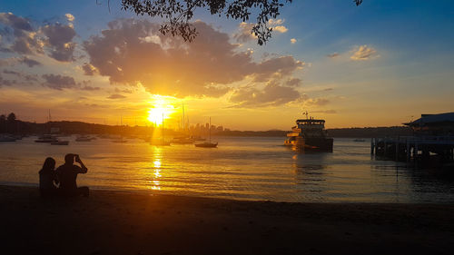 People sitting on beach against sky during sunset