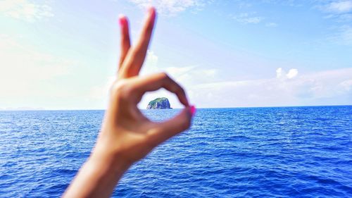 Close-up of hand against sea against sky