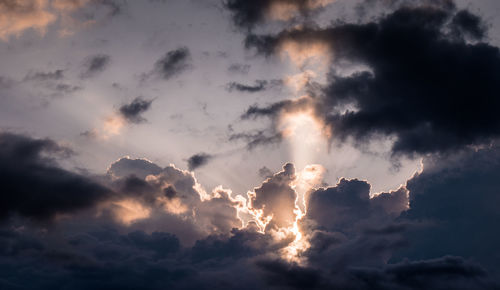 Low angle view of sunlight streaming through clouds during sunset