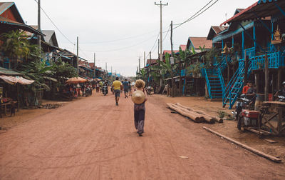 Rear view of woman walking on road against sky in city